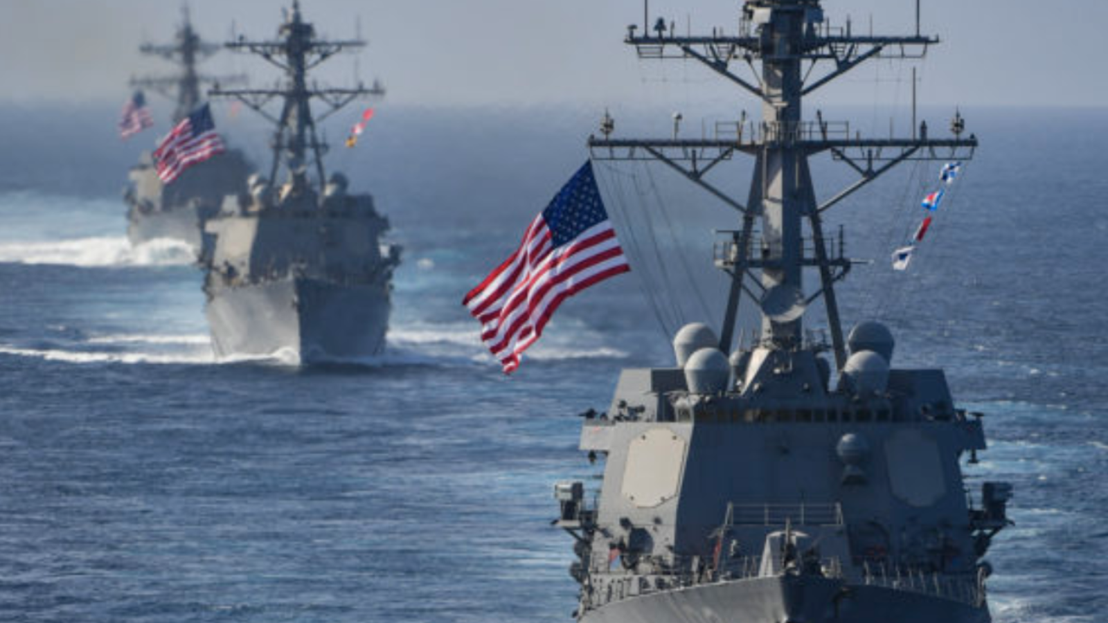 Three Navy destroyers flying American flags at sea