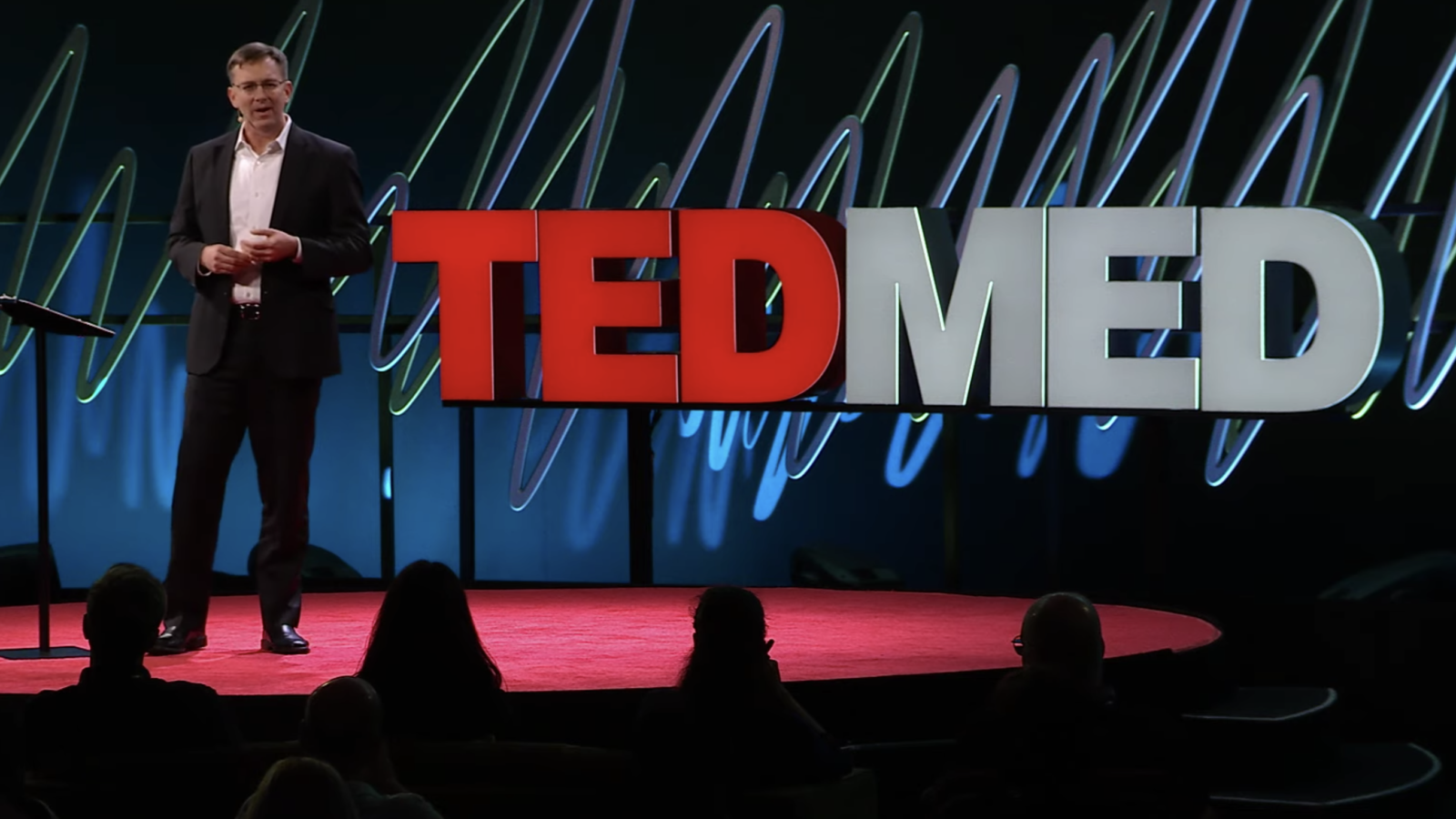 Professor Matthew Hepburn stands in front of a TedMed logo