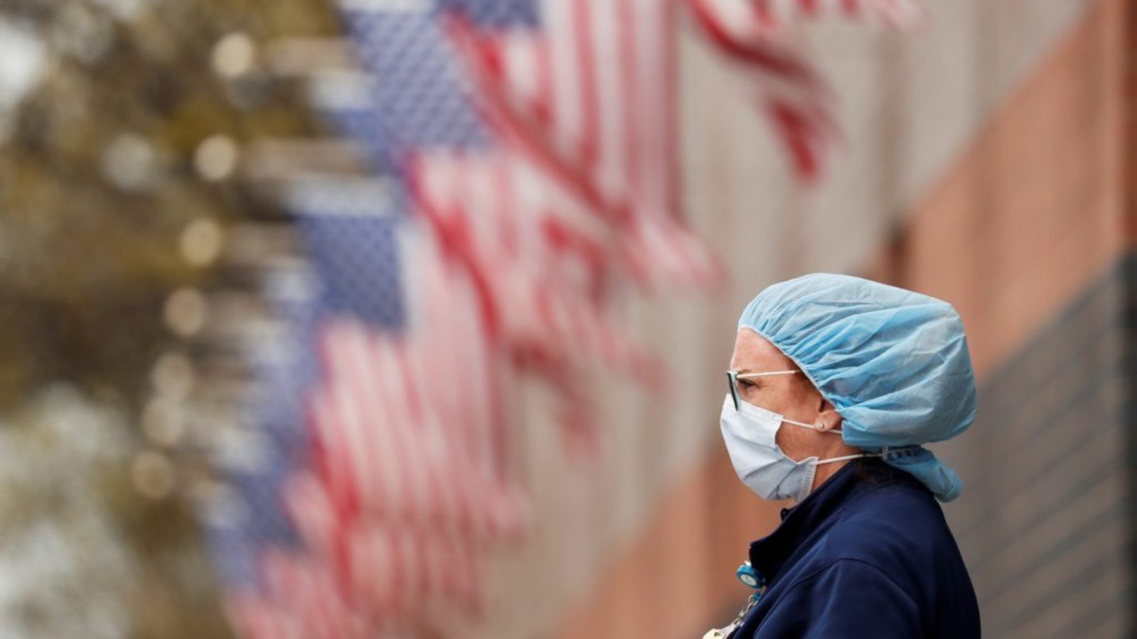 A nurse wearing personal protective equipment in front of a row of American flags