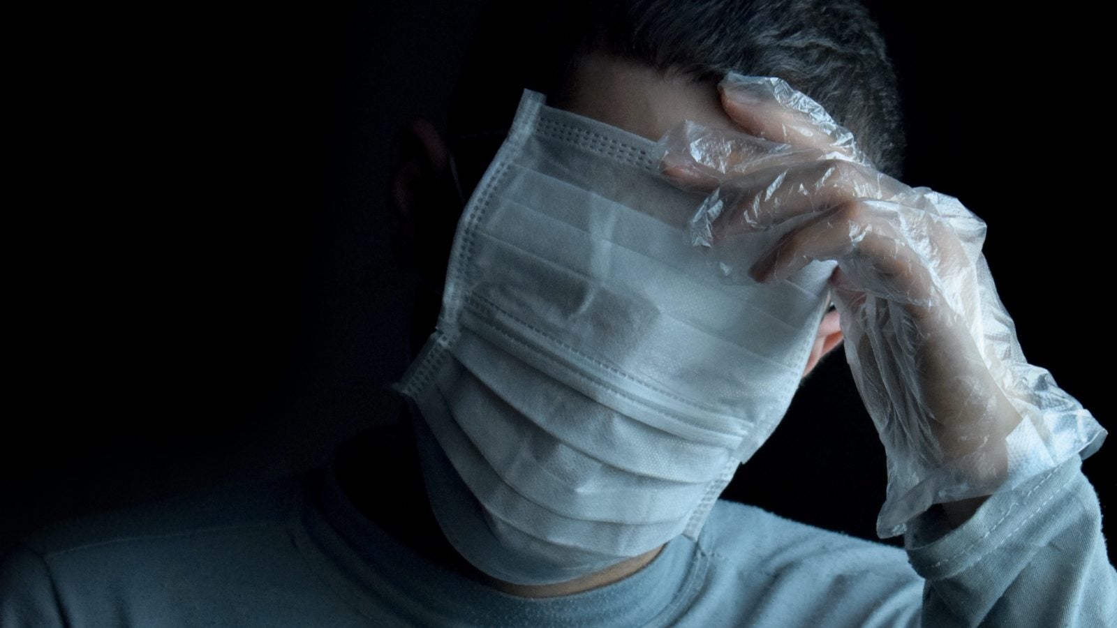 A man wears two face masks that cover his face and eyes in front of a black background.