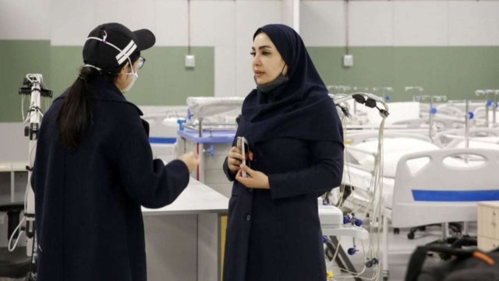 Women in black clothing speak in front of empty hospital beds