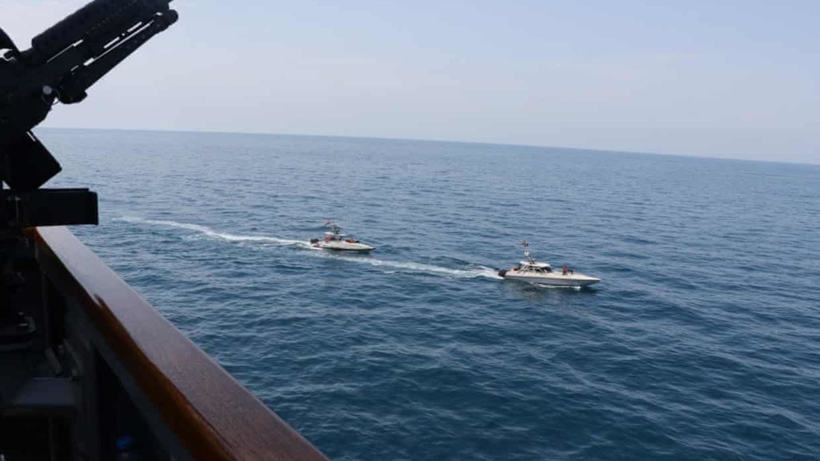 Two small Iranian vessels sail close to a U.S. Navy ship