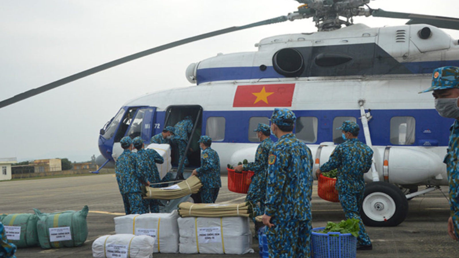 Soldiers in blue camouflage load supplies onto a helicopter with the Vietnamese flag