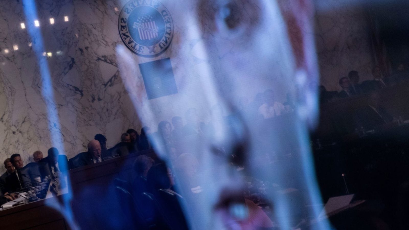 A large image of Mark Zuckerberg is superimposed on the background of a U.S. Senate hearing