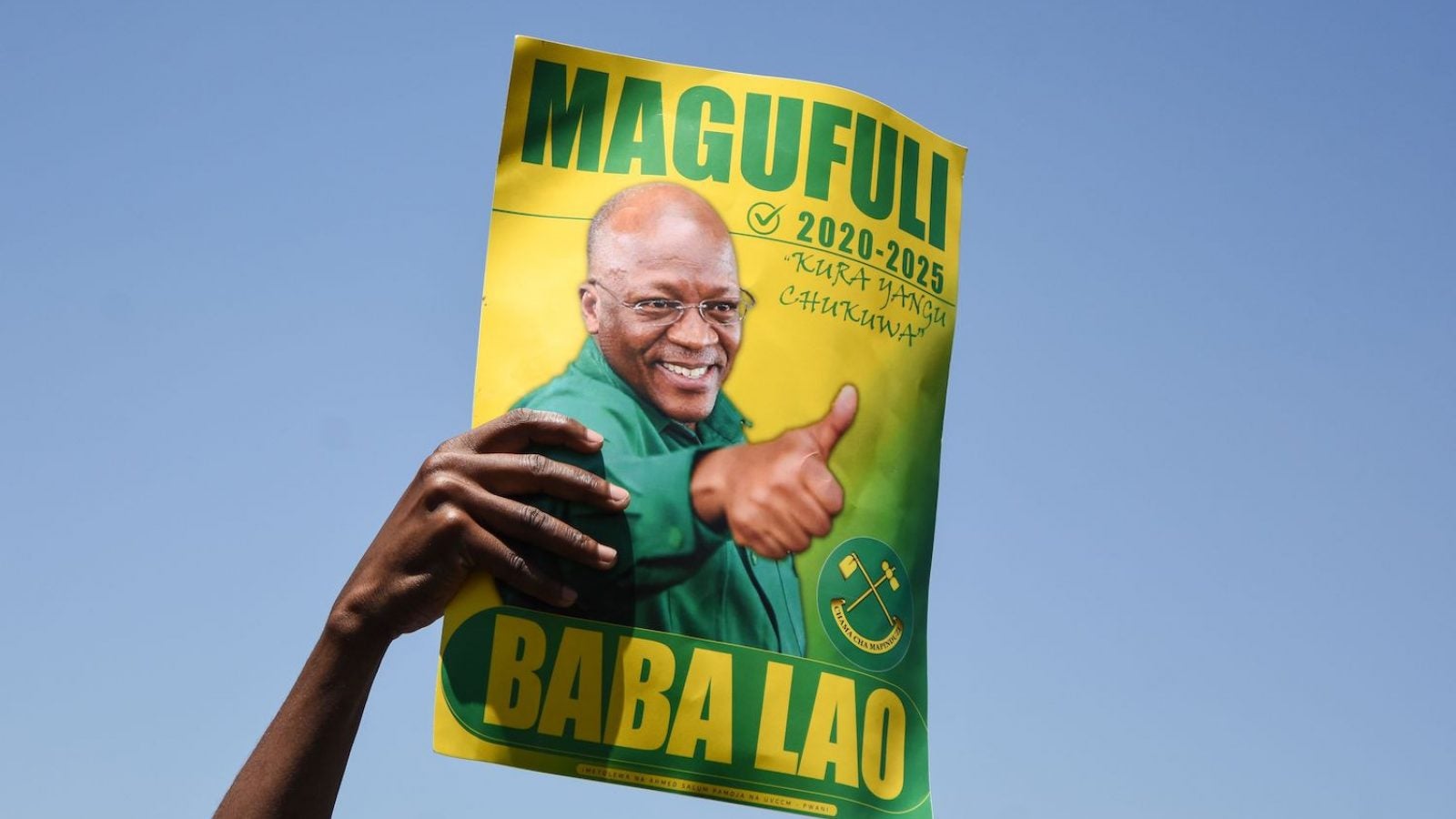 A hand holds up a green and yellow sign that shows John Magufuli