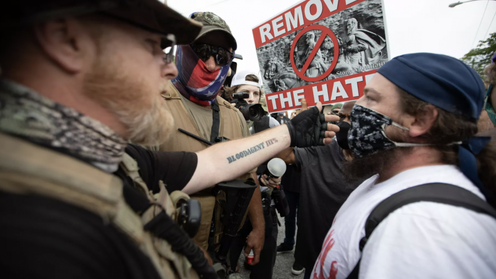 A lgroup of male protestors confront each other, with one carrying a sign that says &quot;Remove the Hate.&quot;