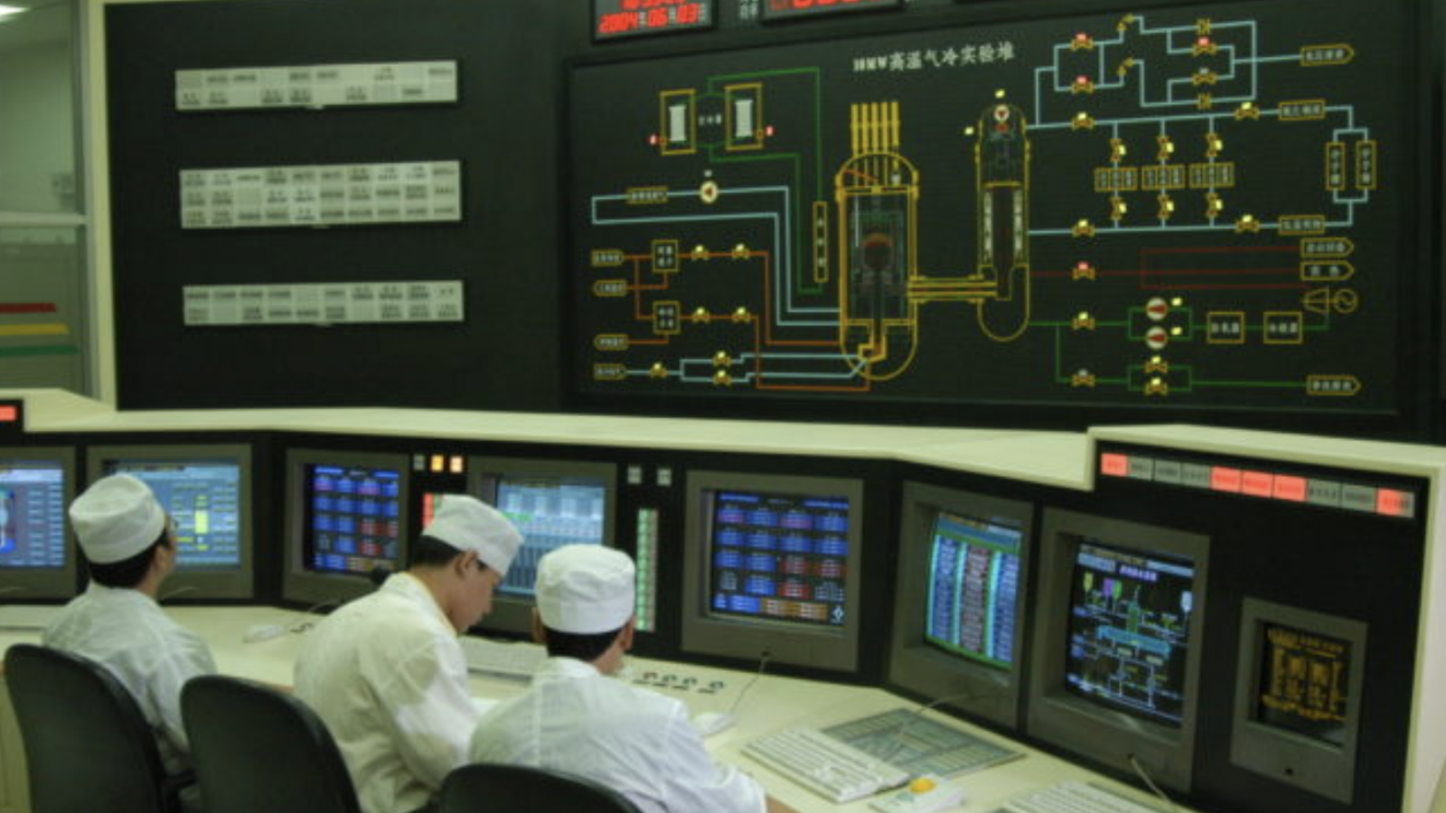 Men in white uniforms sit in front of various computer equipment