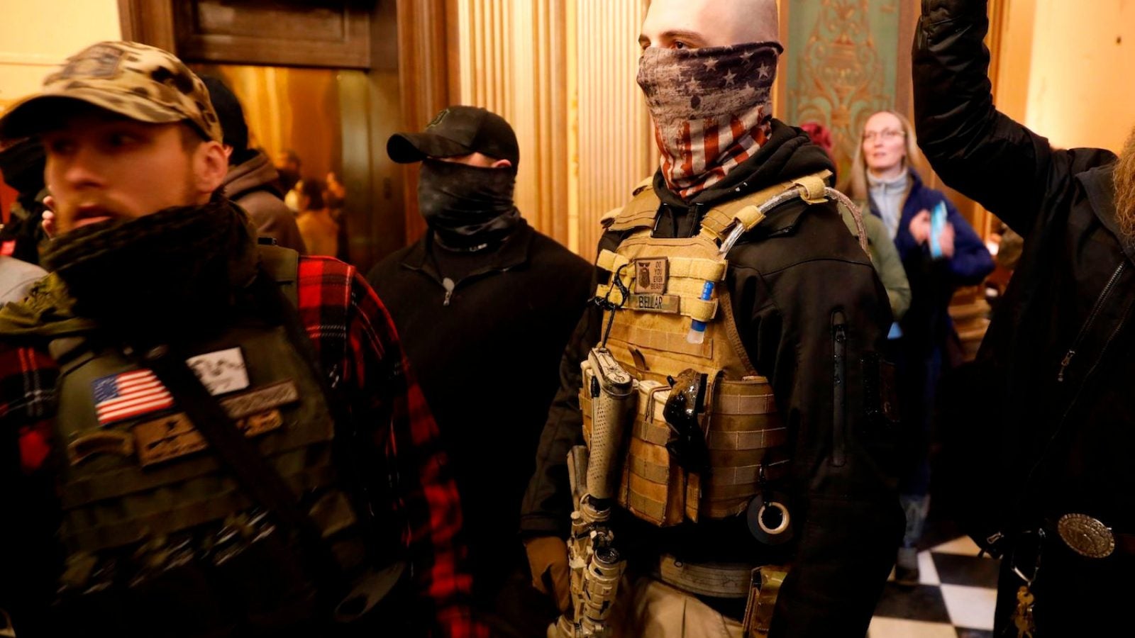 Masked men wearing bulletproof vests stand in a crowd.