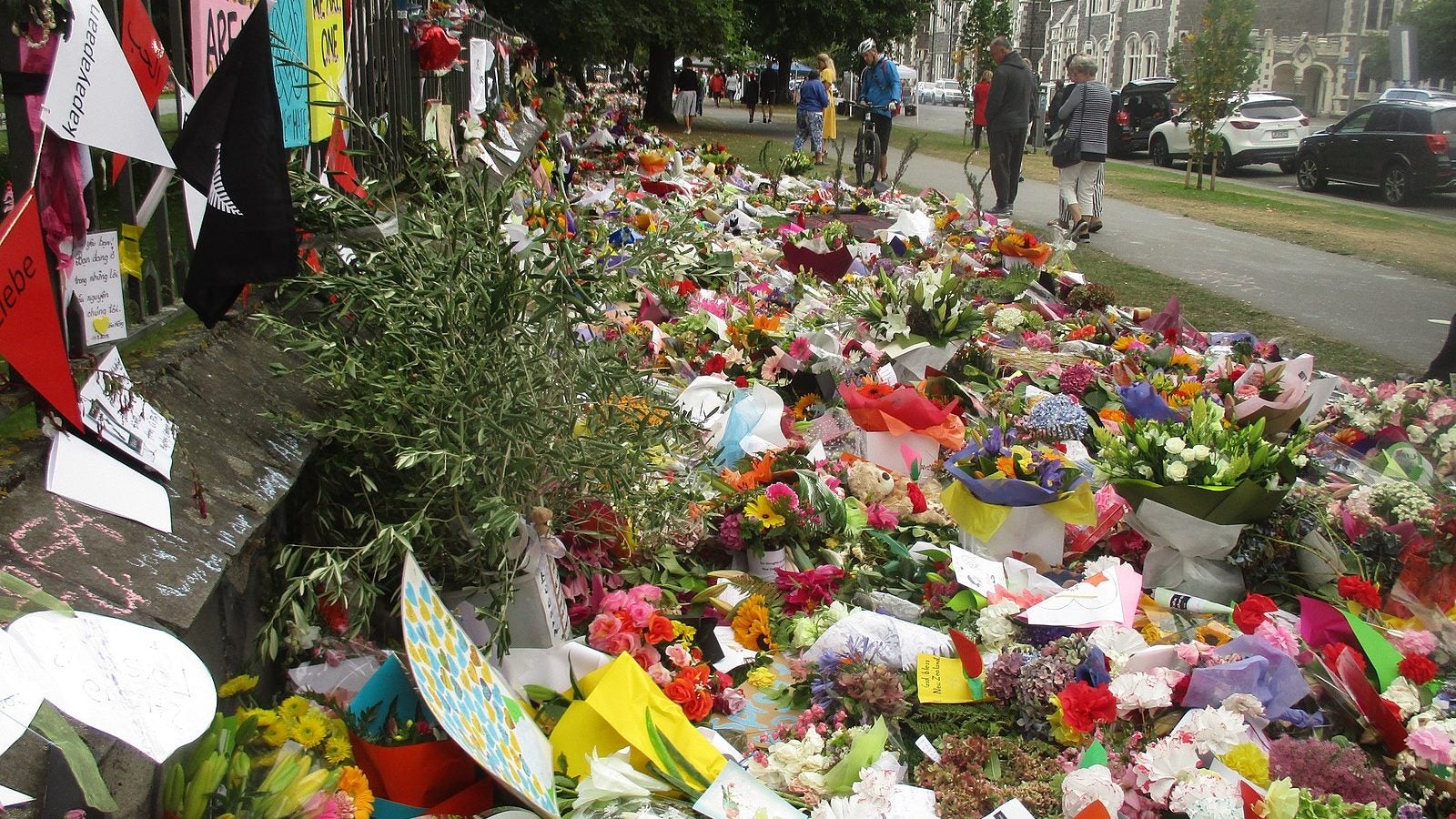 People walk by a large flower memorial