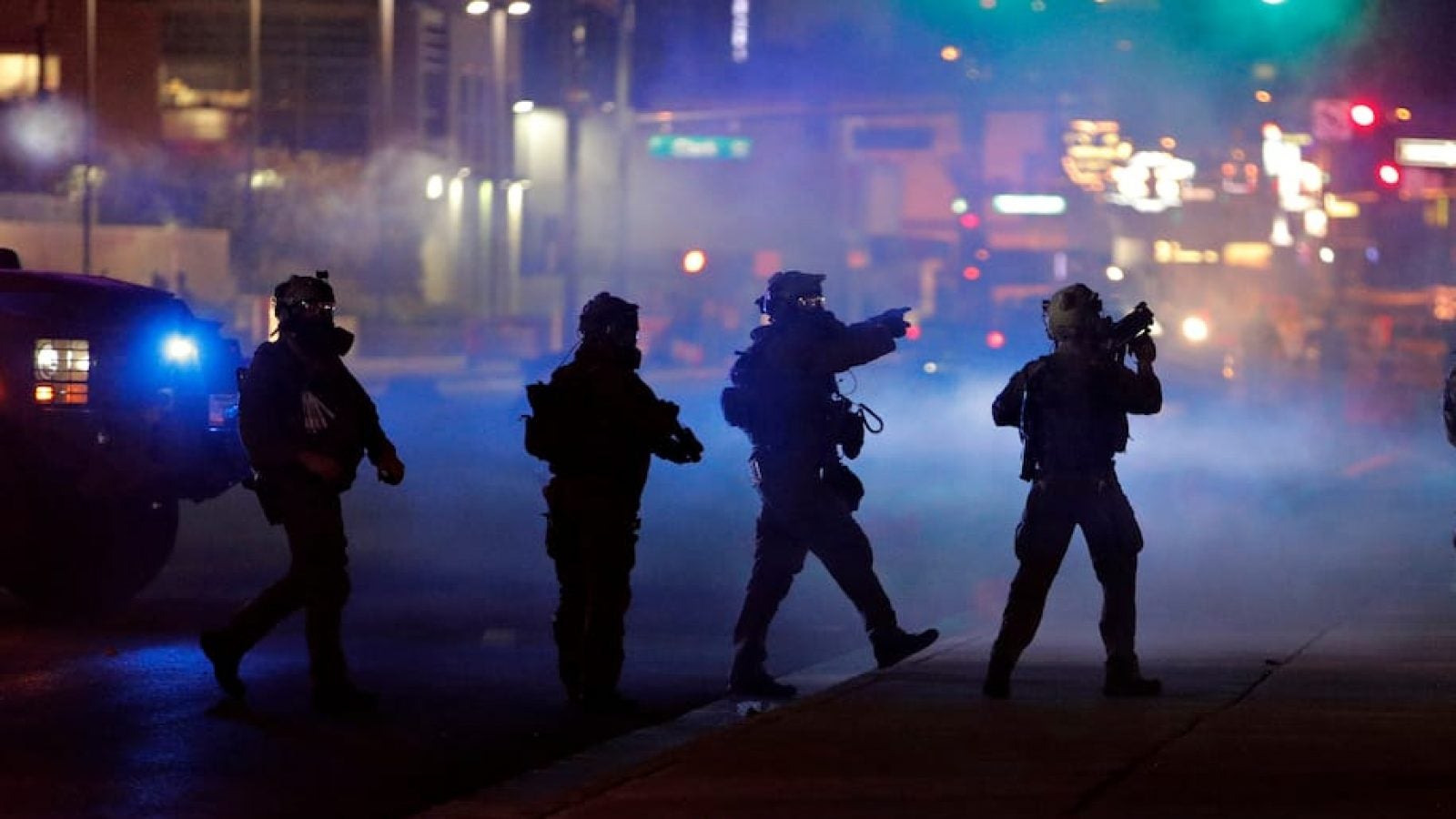 Four police are silhouetted against tear gas and city lights