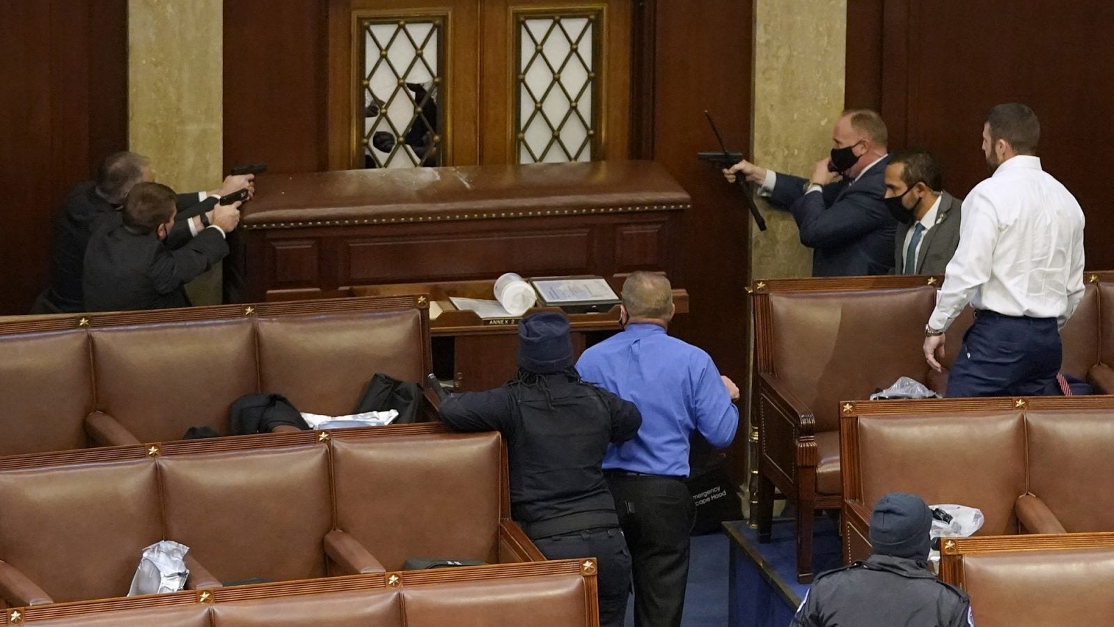 Law enforcement officers point guns at rioters behind a door and barricade in Congress