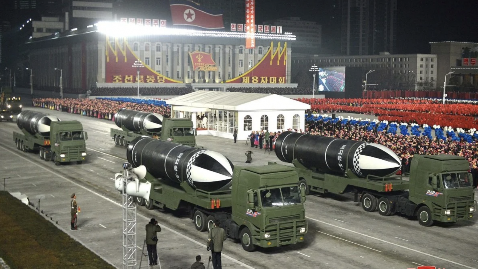 Four green military trucks carrying large submarine launched missiles proceed in a nighttime parade in North Korea.