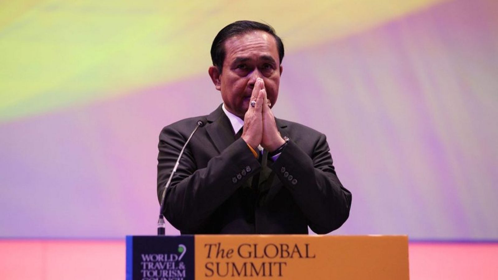 The Thai Prime Minister clasps his hands together behind a podium at The Global Summit in Bangkok