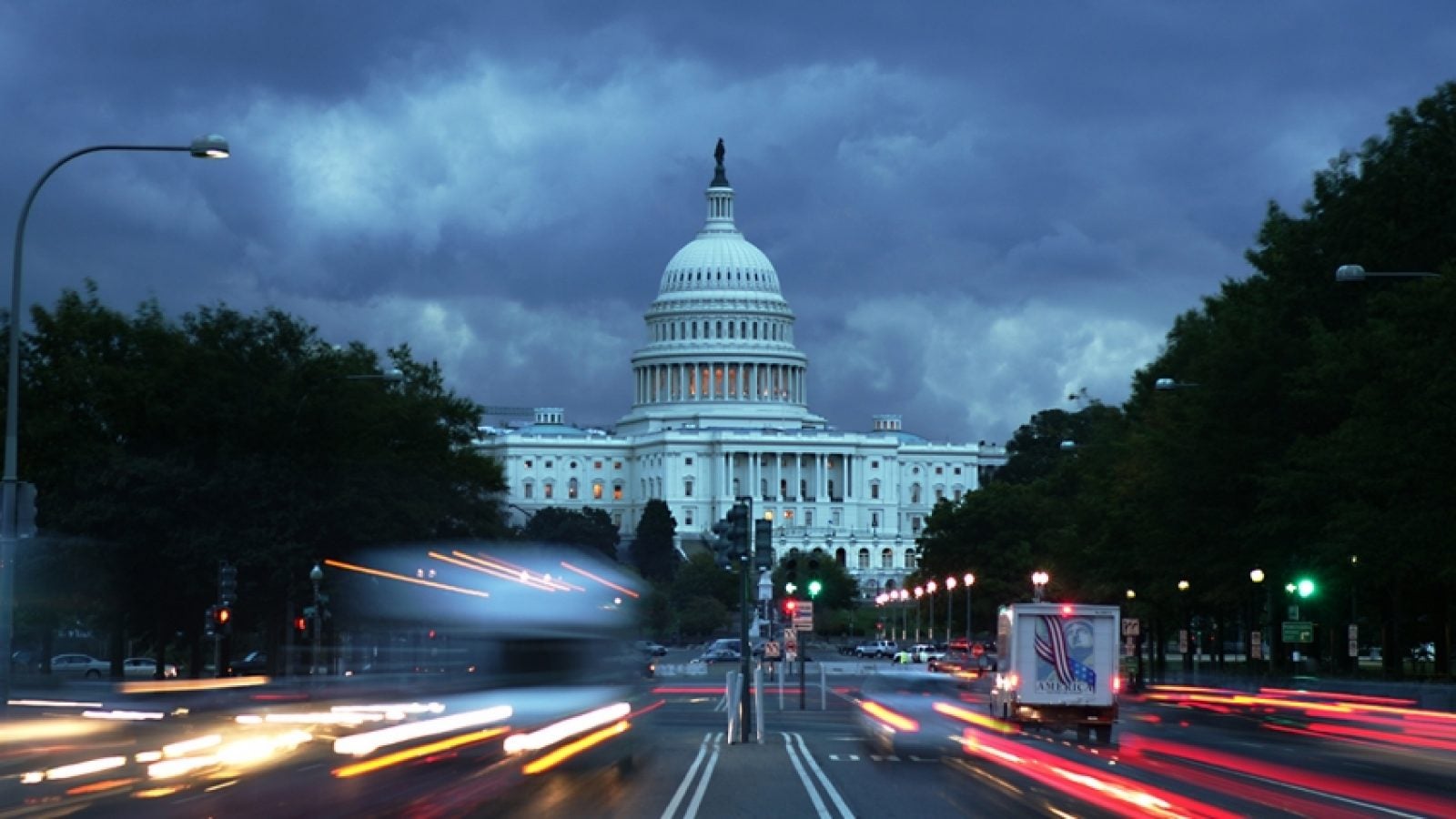 Cars drive in front of the U.S. Capitol Building on a dark stormy evening