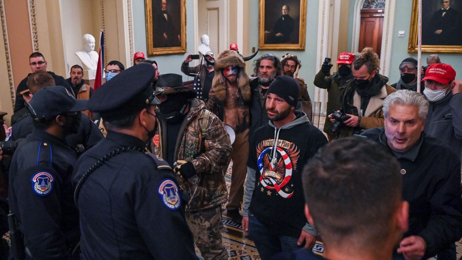 A group of men, some with red MAGA hats and QAnon shirts,face Capitol police inside the Capitol