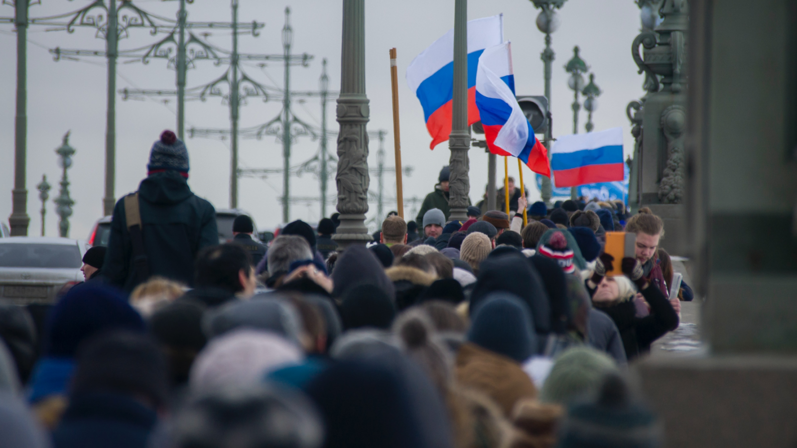 A large crowd of people carrying Russian flags cross a bridge