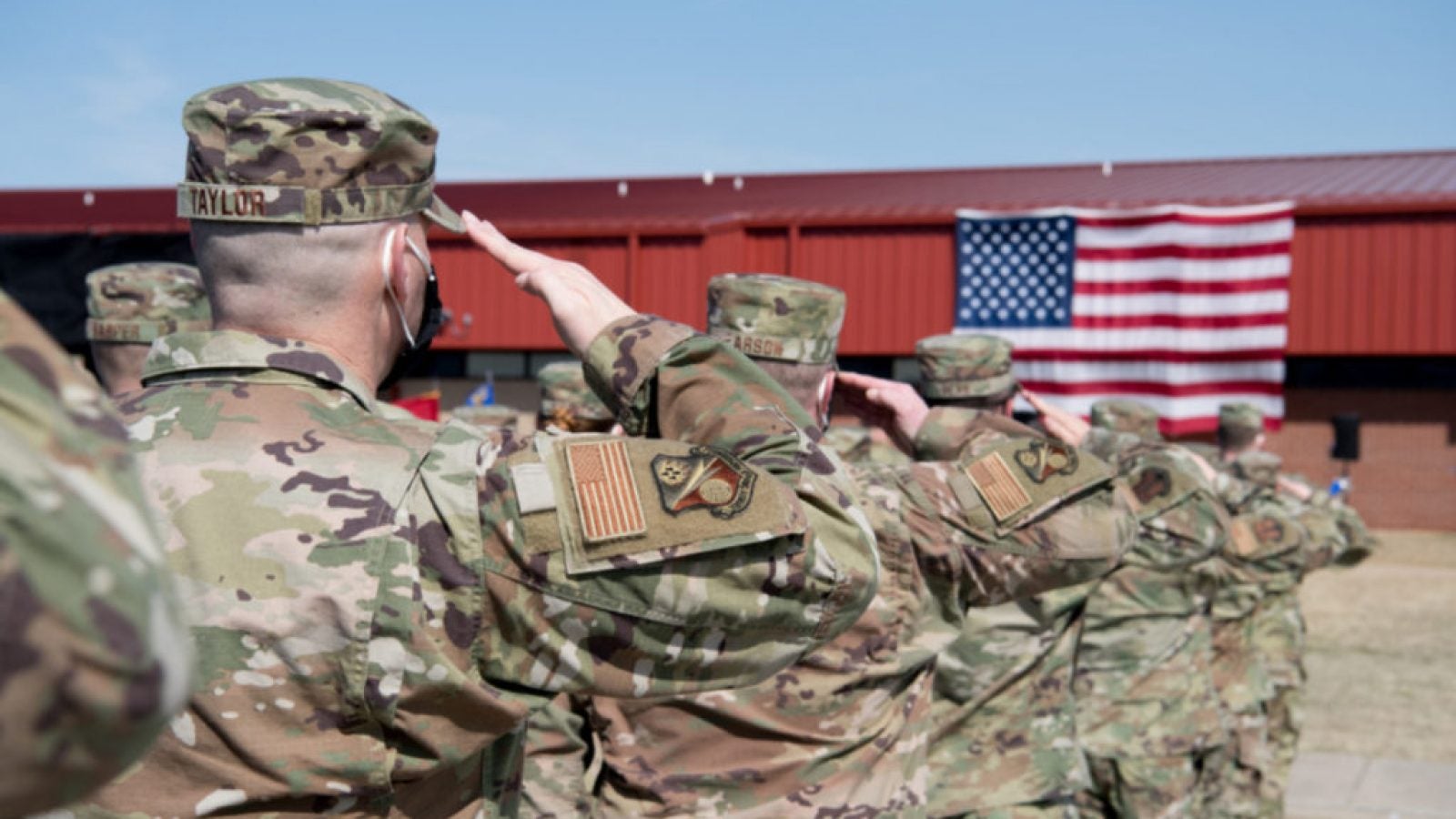 Members of the military in camouflage uniform salute the U.S. flag