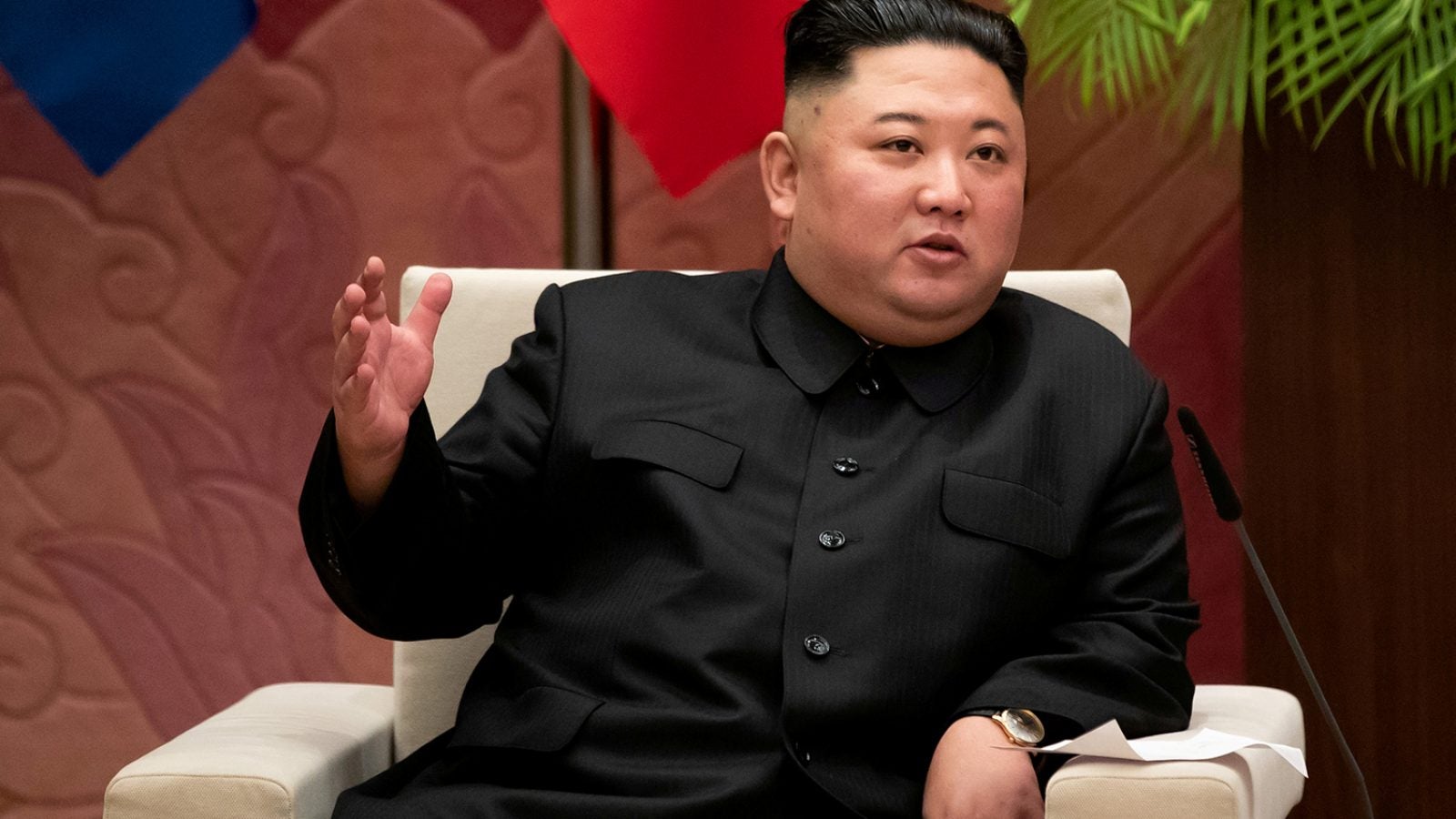 Kim Jong-un gestures with his hand while sitting on a white chair