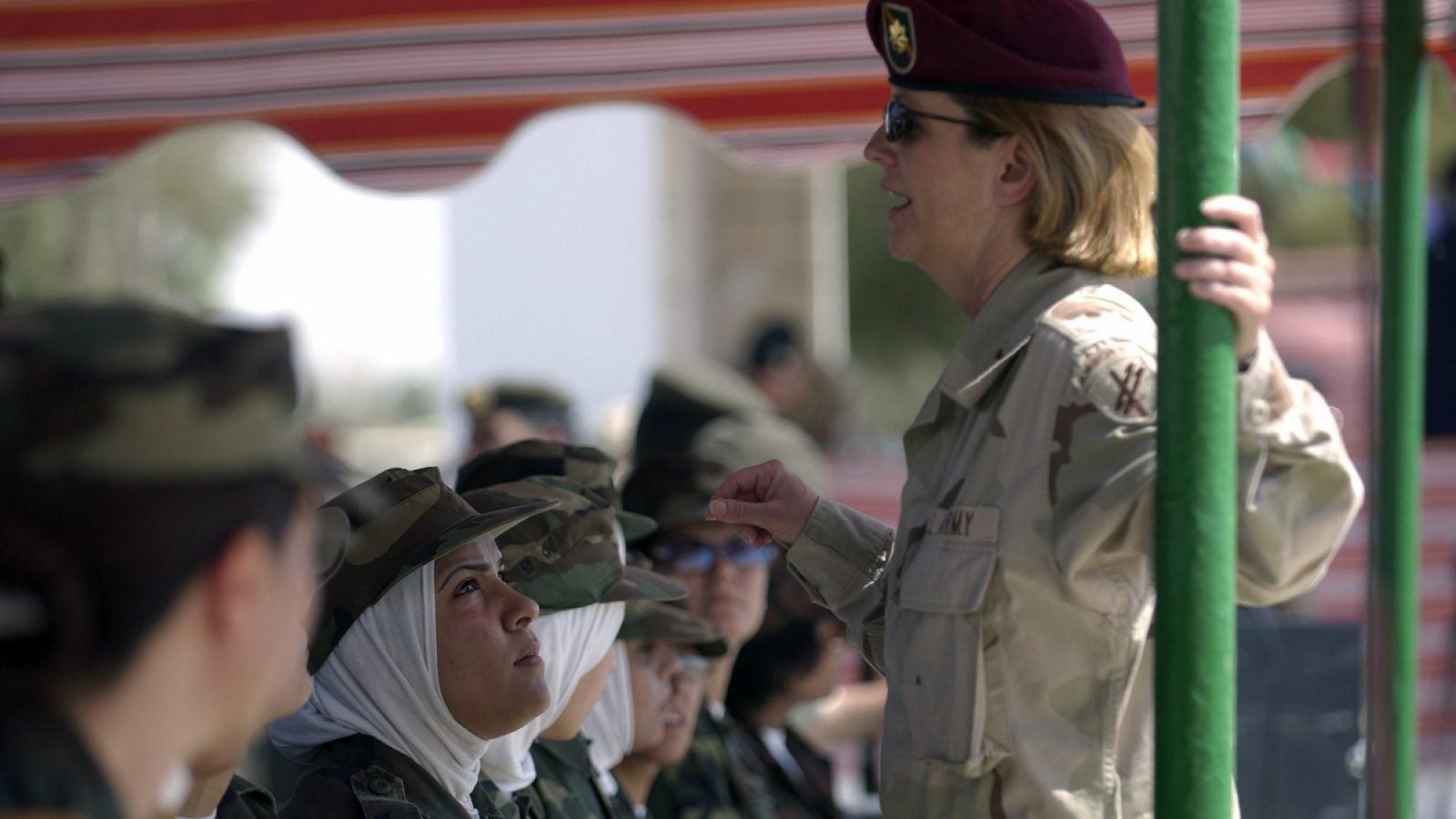 A woman in a green U.S. Army uniform speaks to a group of Iraqi army women