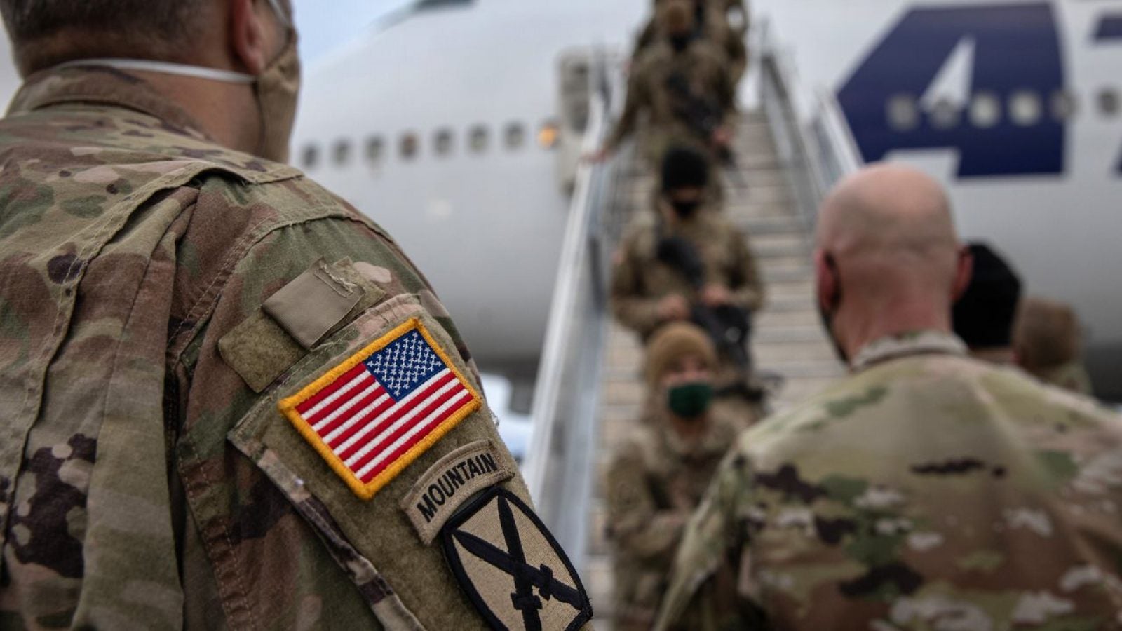 Soldiers in green camouflage board a plane