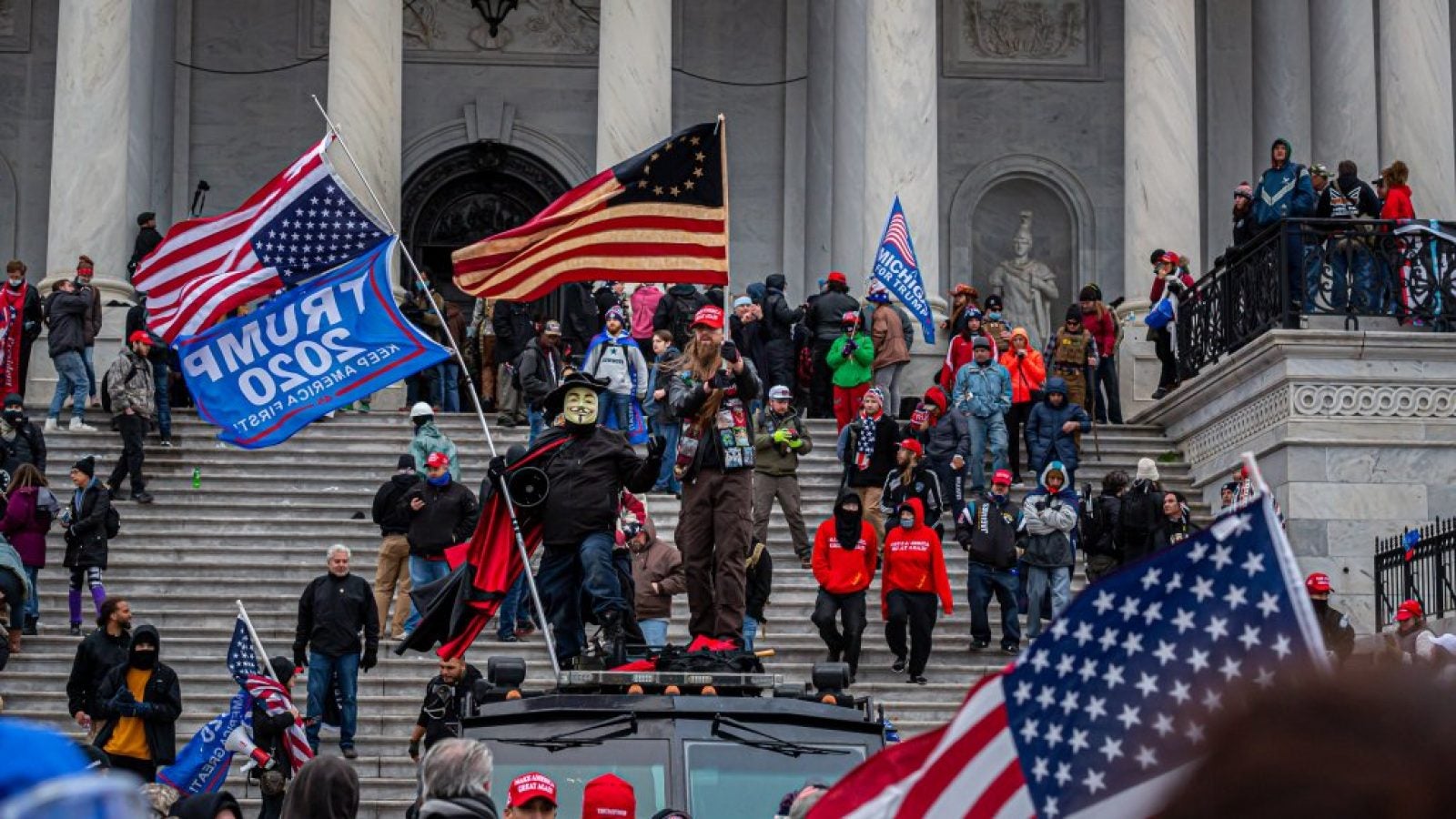 A large crowd of rioters carrying American flags and Trump 2020 flags stand on the U.S. Capitol steps