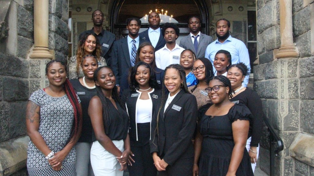 A group of students in professional dress pose on the steps of Healy Hall