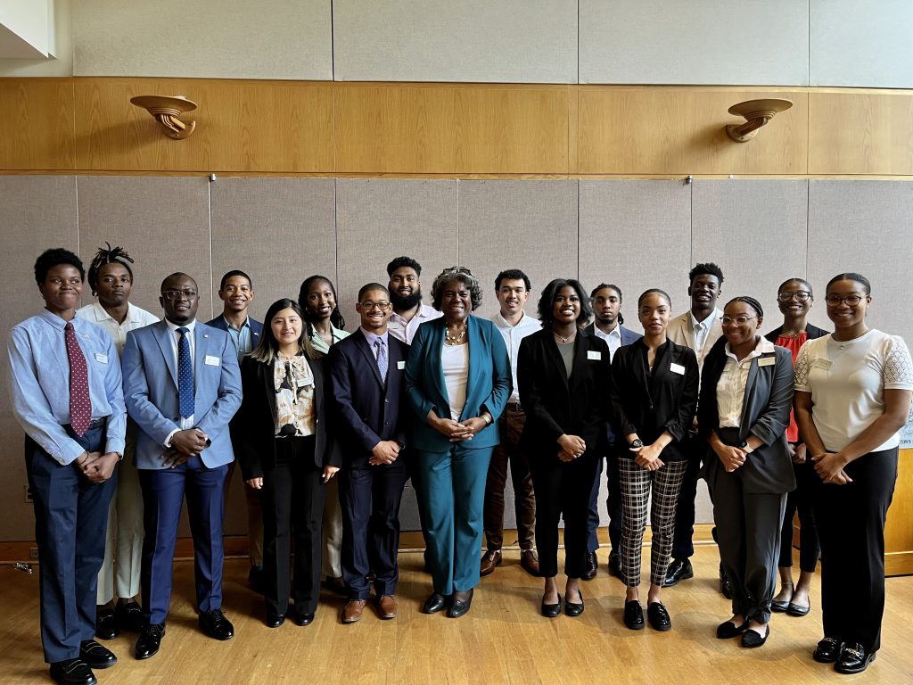 The 16 Summer Institute students stand in a curved line with US Ambassador to the UN, Linda Thomas Greenfield, standing in the middle of the line.